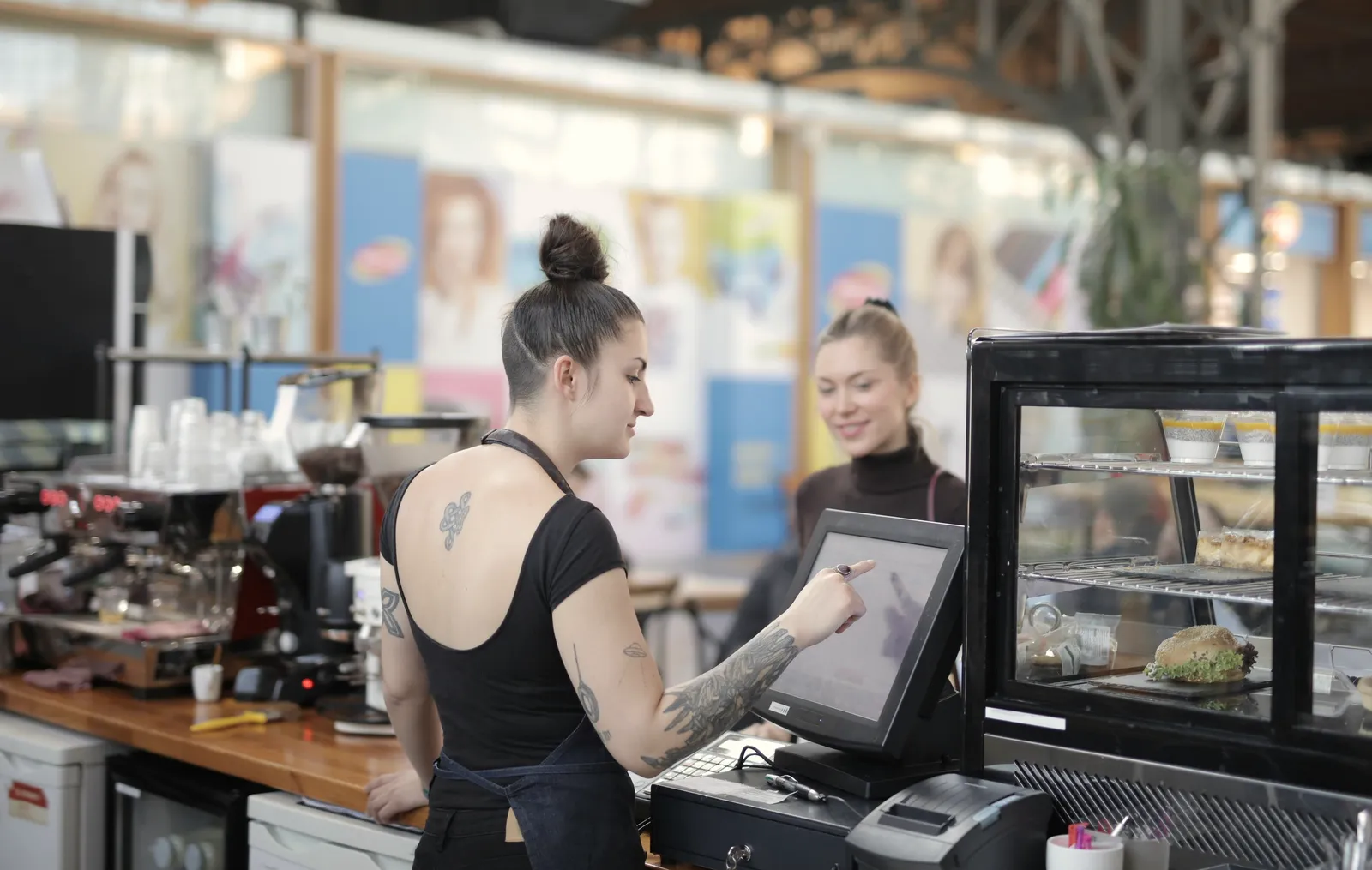 Funcionária de um café a registar um pedido no ecrã tátil do posto de venda, ao balcão, com a colega ao lado